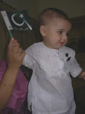 baby in white garment holds flag with crescent moon and star